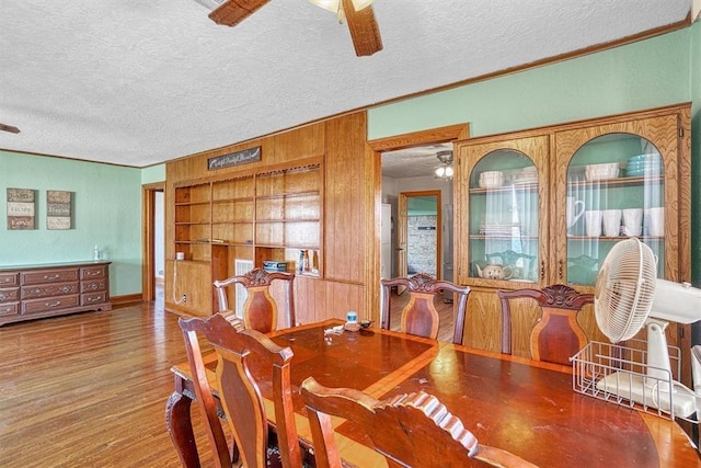dining area featuring wooden walls, a ceiling fan, a textured ceiling, and ornamental molding