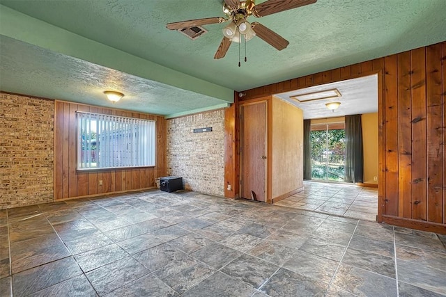 spare room with a textured ceiling, wood walls, stone tile floors, baseboards, and visible vents