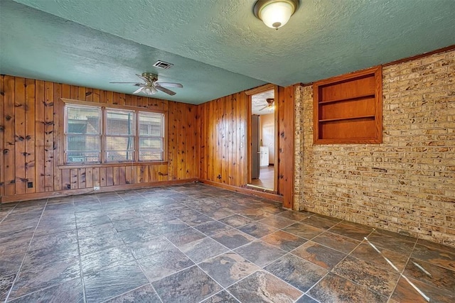 spare room featuring visible vents, wooden walls, a textured ceiling, a ceiling fan, and stone finish flooring