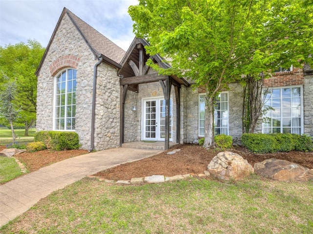 view of front of home with french doors, stone siding, and a front lawn