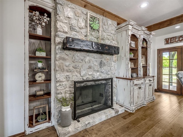 unfurnished living room with beamed ceiling, a stone fireplace, recessed lighting, and wood finished floors