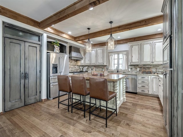 kitchen with backsplash, beam ceiling, premium range hood, and stainless steel appliances