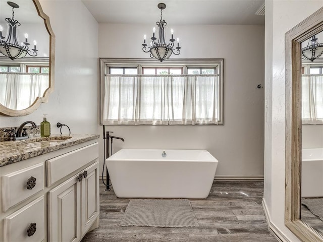 full bathroom with a freestanding tub, vanity, wood finished floors, and a notable chandelier