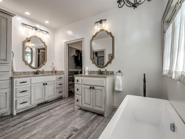 bathroom with a freestanding tub, recessed lighting, wood finished floors, and two vanities