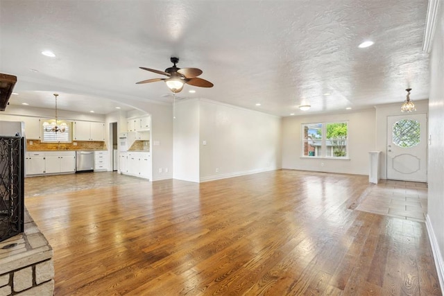 unfurnished living room featuring arched walkways, baseboards, ceiling fan with notable chandelier, light wood finished floors, and recessed lighting