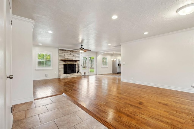 unfurnished living room featuring a stone fireplace, baseboards, ceiling fan with notable chandelier, ornamental molding, and recessed lighting