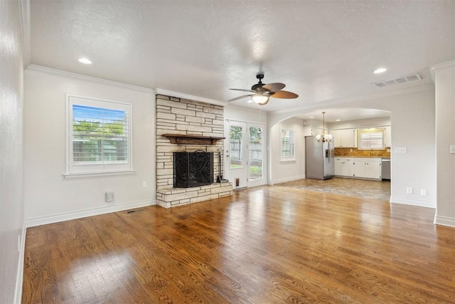 unfurnished living room with a stone fireplace, arched walkways, baseboards, ceiling fan with notable chandelier, and ornamental molding