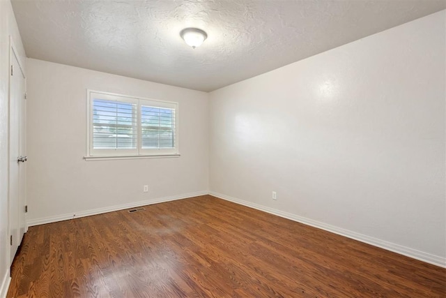 empty room featuring visible vents, a textured ceiling, baseboards, and wood finished floors