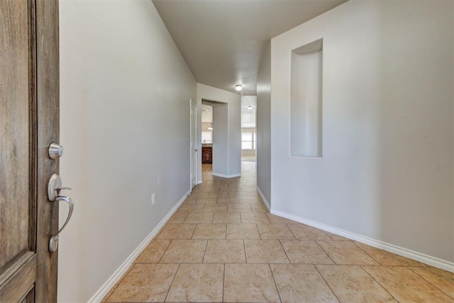 hall featuring light tile patterned floors and baseboards