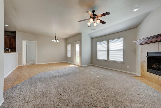 unfurnished living room with a tiled fireplace, a chandelier, ceiling fan, baseboards, and tile patterned flooring