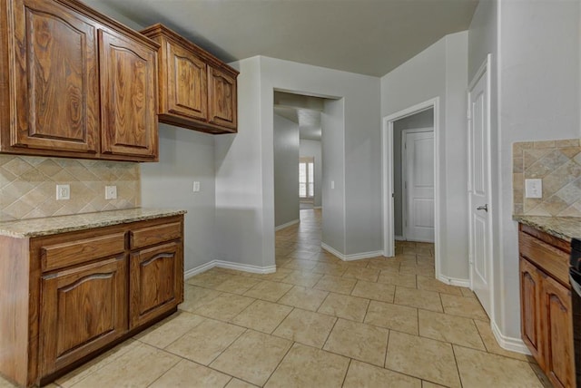 kitchen featuring tasteful backsplash, light stone counters, and brown cabinetry