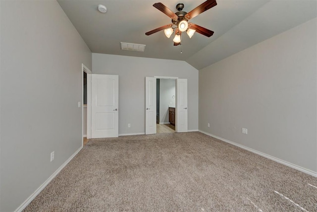 unfurnished bedroom featuring light carpet, lofted ceiling, baseboards, ensuite bath, and a ceiling fan