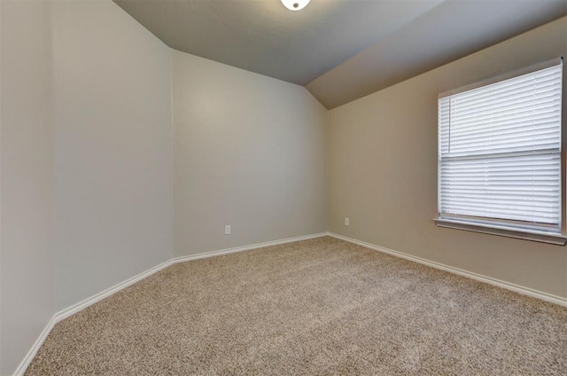 spare room featuring carpet floors, lofted ceiling, and baseboards