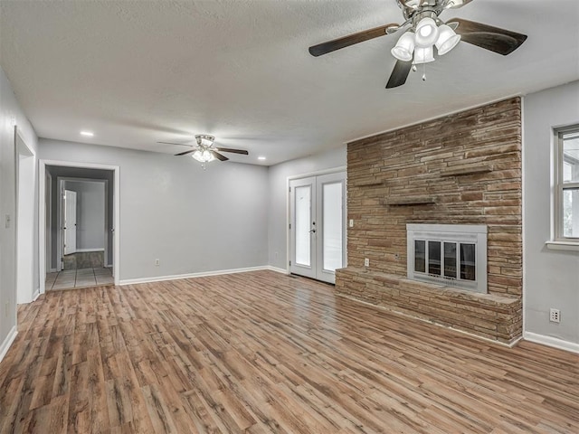 unfurnished living room featuring wood finished floors, a fireplace, baseboards, a textured ceiling, and a ceiling fan