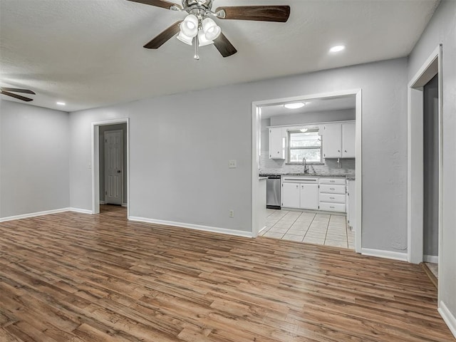 unfurnished living room with baseboards, ceiling fan, a sink, and light wood-style flooring