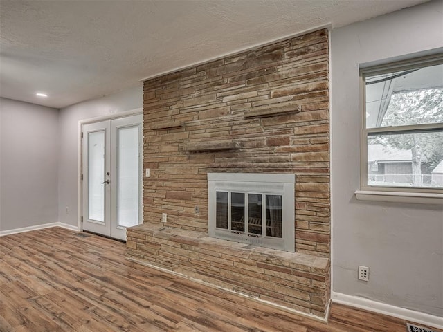 unfurnished living room with french doors, a stone fireplace, a textured ceiling, wood finished floors, and baseboards