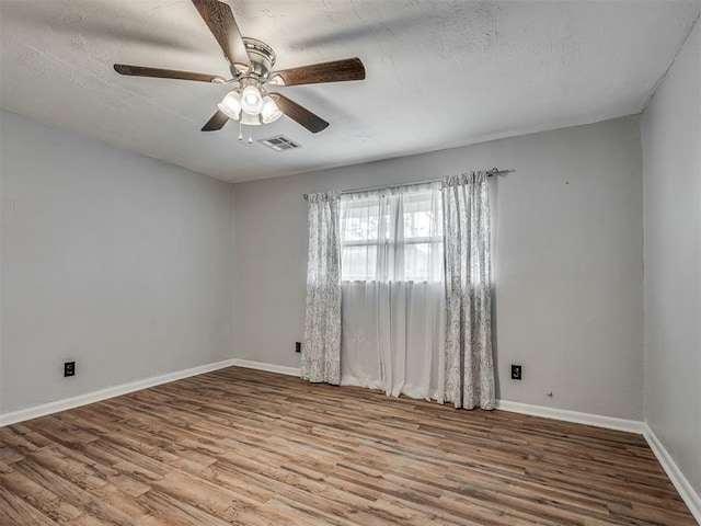 empty room with a textured ceiling, a ceiling fan, baseboards, wood finished floors, and visible vents