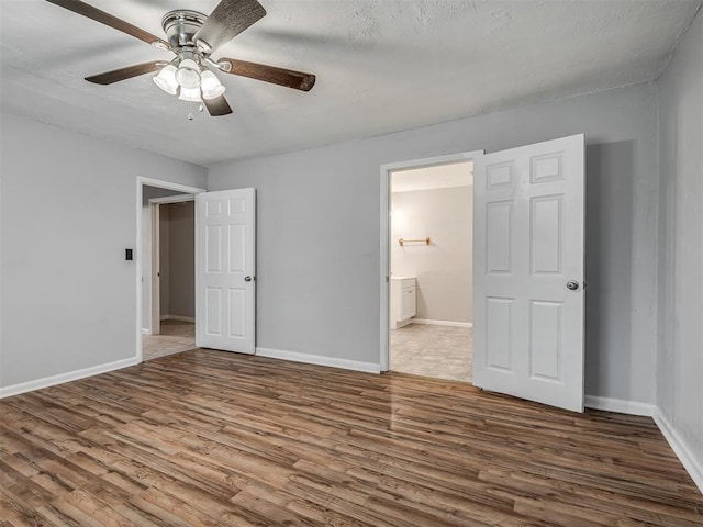 unfurnished bedroom with baseboards, a ceiling fan, ensuite bath, and wood finished floors