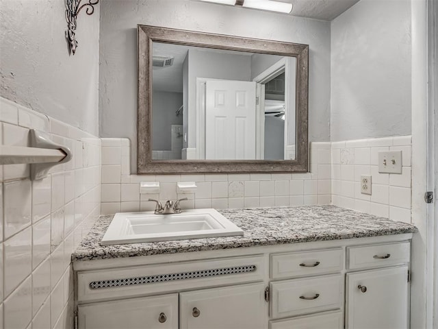bathroom with backsplash, a textured wall, tile walls, and vanity