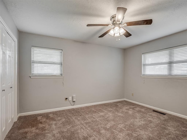 carpeted empty room with plenty of natural light, a textured ceiling, and visible vents