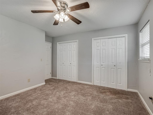 unfurnished bedroom with carpet floors, a textured ceiling, baseboards, and two closets