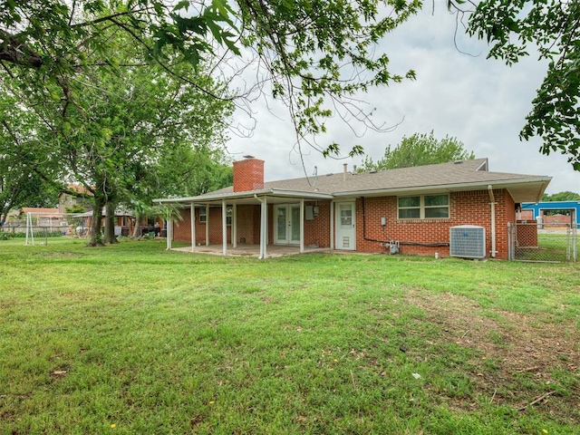 back of house with fence, a chimney, brick siding, central air condition unit, and a yard