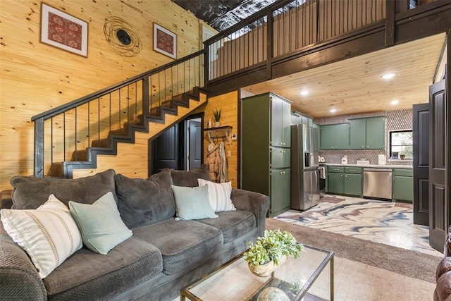 living room with a high ceiling, light carpet, wood walls, stairs, and recessed lighting