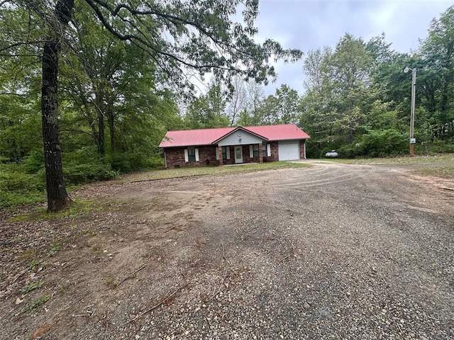 ranch-style home with dirt driveway, an attached garage, and metal roof