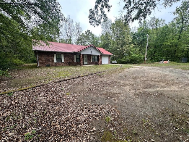 ranch-style house with dirt driveway, brick siding, metal roof, and a garage