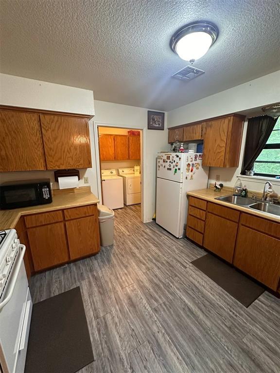 kitchen featuring a sink, white appliances, separate washer and dryer, brown cabinetry, and visible vents