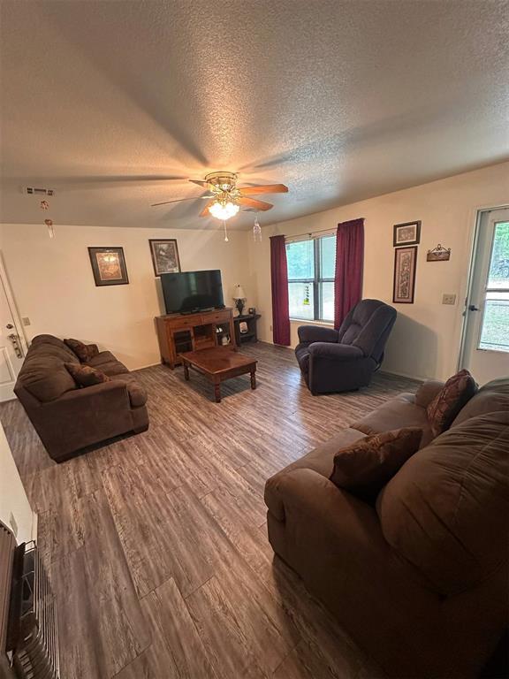 living area with a textured ceiling, ceiling fan, wood finished floors, and a wealth of natural light