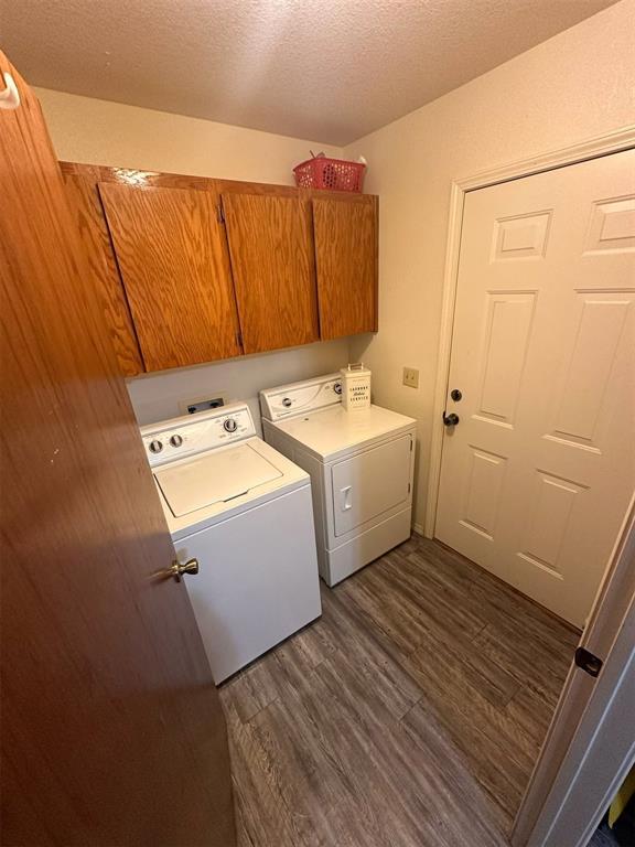 clothes washing area with cabinet space, a textured ceiling, dark wood-style floors, and washer and dryer