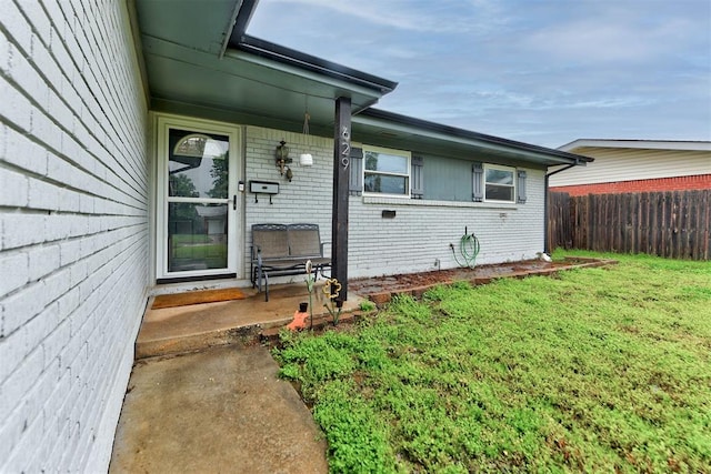 entrance to property featuring a lawn, brick siding, and fence