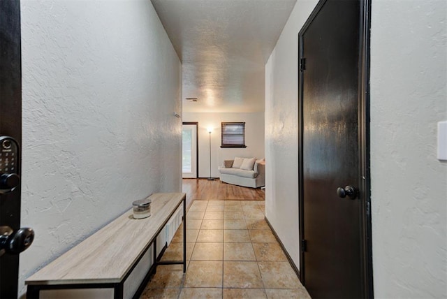hallway with baseboards, a textured wall, and light tile patterned floors