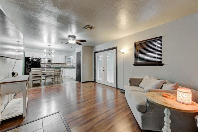 living area with ceiling fan with notable chandelier, dark wood-style flooring, a textured ceiling, and visible vents