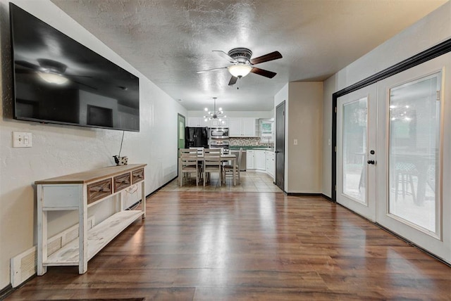 interior space with a textured ceiling, french doors, ceiling fan with notable chandelier, visible vents, and dark wood-style floors