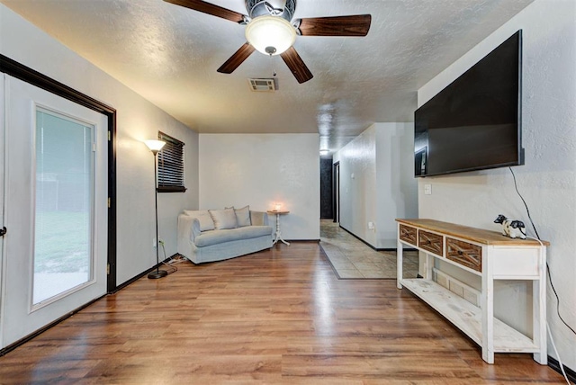 living room featuring a ceiling fan, a textured ceiling, visible vents, and light wood-style flooring