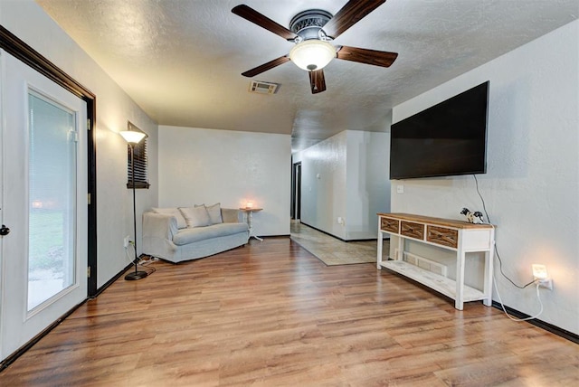 living room with visible vents, baseboards, a textured ceiling, a ceiling fan, and light wood finished floors