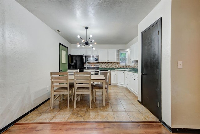 kitchen featuring white cabinetry, a sink, appliances with stainless steel finishes, backsplash, and a notable chandelier
