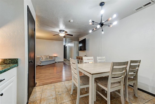 dining room featuring a textured ceiling, visible vents, light tile patterned floors, and ceiling fan with notable chandelier
