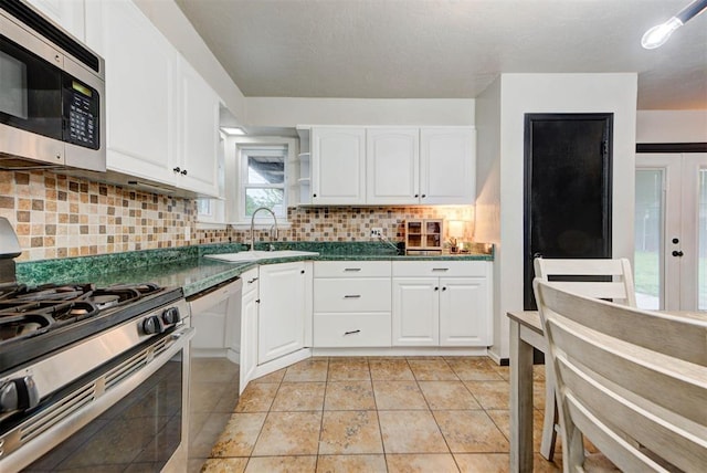 kitchen featuring white cabinets, stainless steel appliances, dark countertops, and a sink
