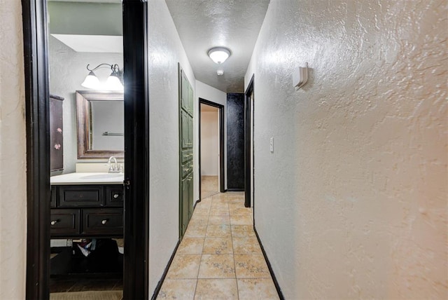 corridor featuring a sink, a textured wall, and a textured ceiling