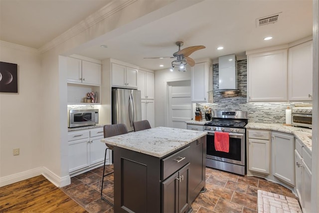 kitchen featuring white cabinets, appliances with stainless steel finishes, wall chimney exhaust hood, a center island, and decorative backsplash