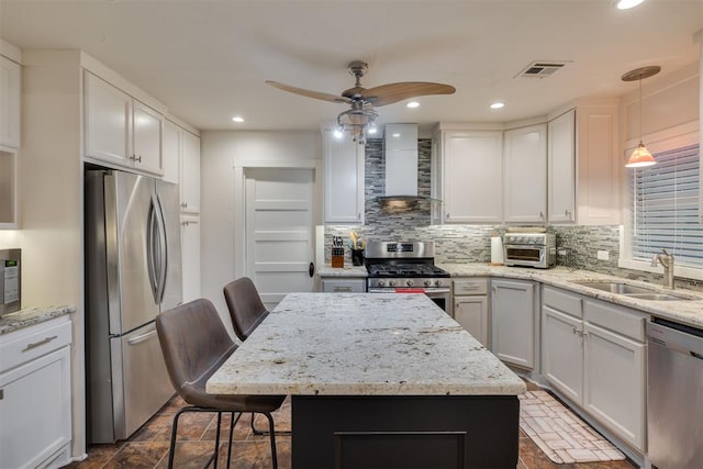 kitchen with wall chimney range hood, ceiling fan, visible vents, appliances with stainless steel finishes, and a sink
