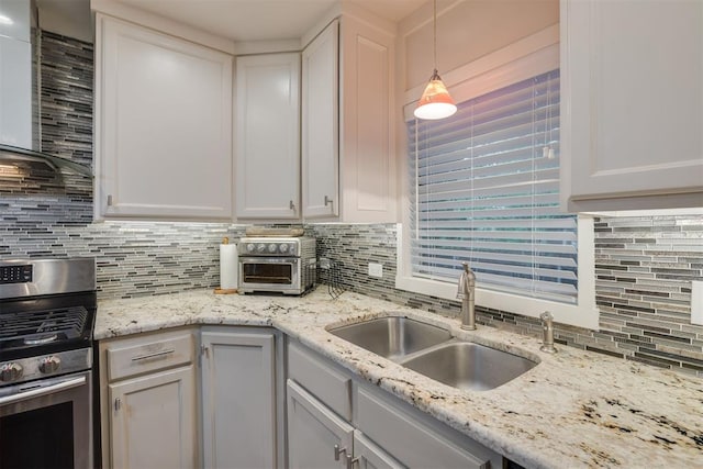 kitchen with wall chimney range hood, hanging light fixtures, a sink, stainless steel range with gas stovetop, and decorative backsplash