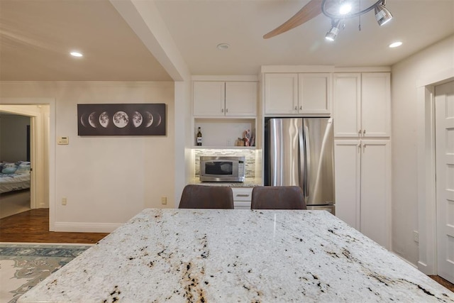 kitchen featuring baseboards, ceiling fan, white cabinetry, light stone counters, and stainless steel appliances
