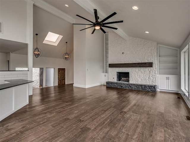 unfurnished living room featuring dark wood-style flooring, beamed ceiling, a stone fireplace, a ceiling fan, and a skylight