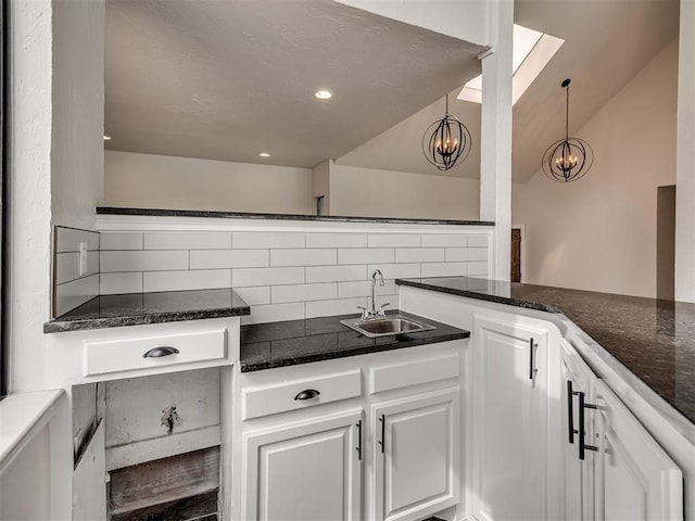 kitchen featuring white cabinets, a notable chandelier, a sink, dark stone counters, and decorative backsplash