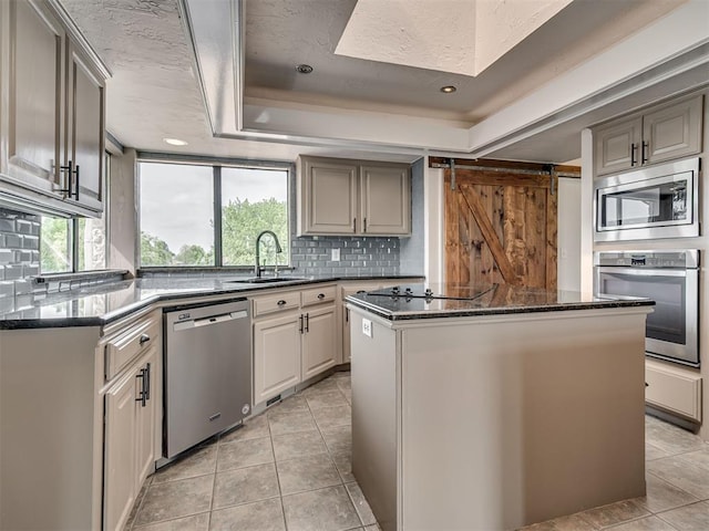 kitchen featuring backsplash, appliances with stainless steel finishes, a center island, a sink, and a raised ceiling