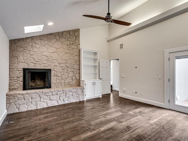 unfurnished living room with visible vents, dark wood-style flooring, baseboards, a stone fireplace, and ceiling fan